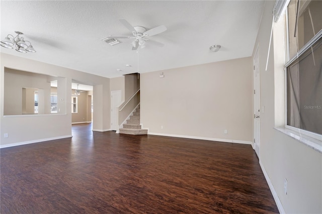 spare room with ceiling fan with notable chandelier, visible vents, baseboards, stairs, and dark wood-style floors