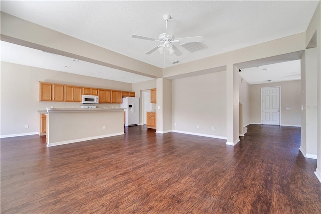 unfurnished living room featuring visible vents, dark wood finished floors, baseboards, and ceiling fan