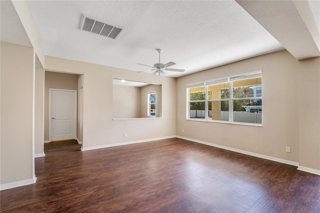 spare room with a textured ceiling, dark wood-style flooring, a ceiling fan, visible vents, and baseboards