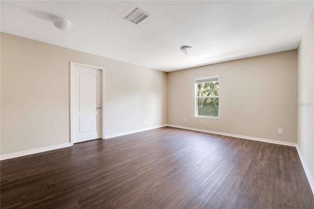 empty room with a textured ceiling, dark wood-style flooring, visible vents, and baseboards