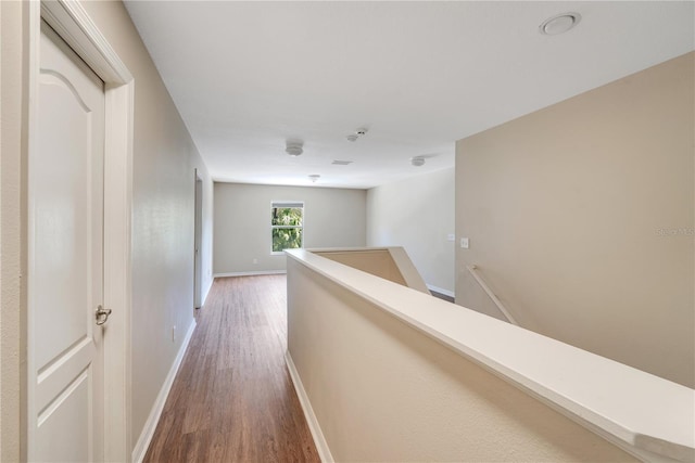 hall featuring baseboards, wood finished floors, and an upstairs landing