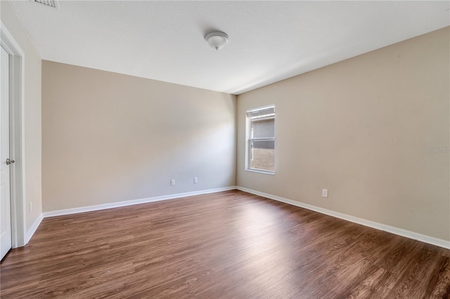 spare room featuring baseboards and dark wood-type flooring