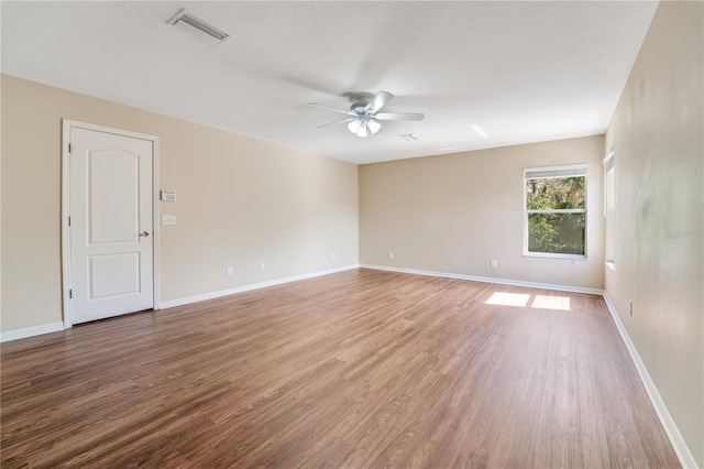 unfurnished room with ceiling fan, wood finished floors, visible vents, and baseboards