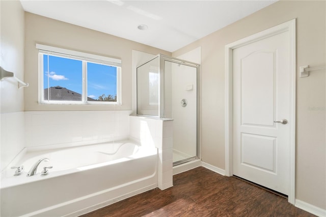 bathroom with a bath, a shower stall, baseboards, and wood finished floors