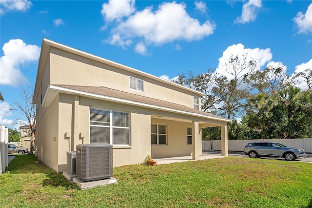 back of property with central AC unit, a lawn, fence, and stucco siding