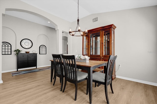 dining room featuring lofted ceiling, light wood finished floors, baseboards, and a notable chandelier