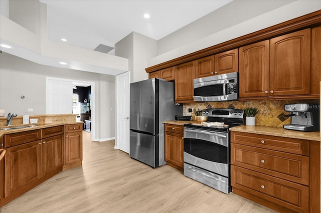 kitchen featuring stainless steel appliances, brown cabinetry, a sink, and light stone counters