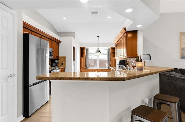 kitchen with a breakfast bar area, stainless steel appliances, a peninsula, brown cabinets, and decorative light fixtures