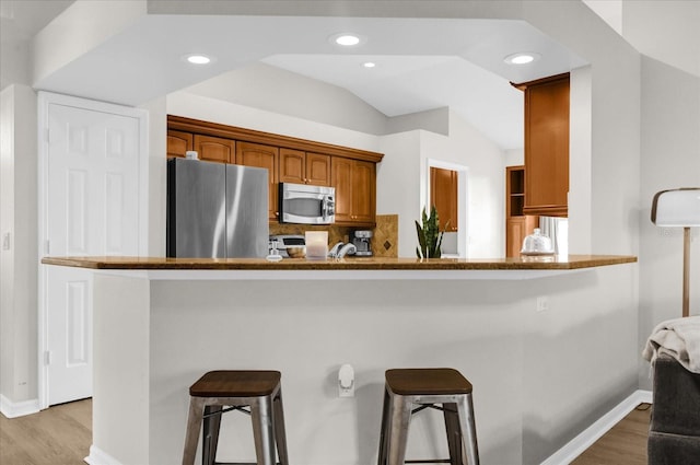 kitchen with lofted ceiling, appliances with stainless steel finishes, light wood-style floors, a peninsula, and a kitchen bar