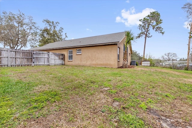 back of house featuring stucco siding, fence, central AC, and a yard