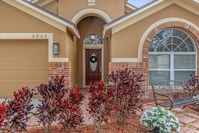 doorway to property featuring brick siding, an attached garage, and stucco siding