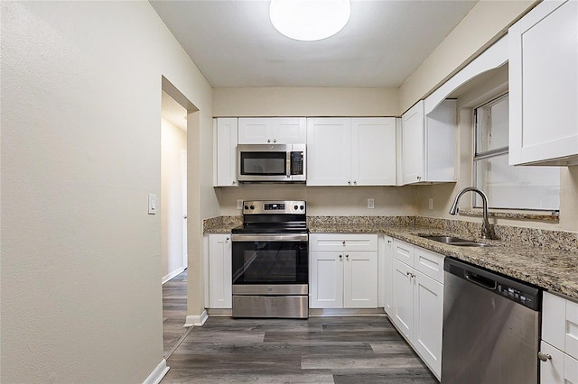 kitchen with stone counters, appliances with stainless steel finishes, white cabinets, and a sink