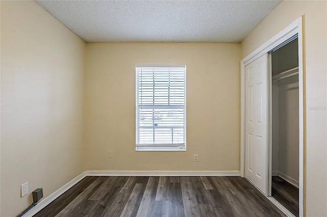 unfurnished bedroom with a textured ceiling, a closet, dark wood finished floors, and baseboards