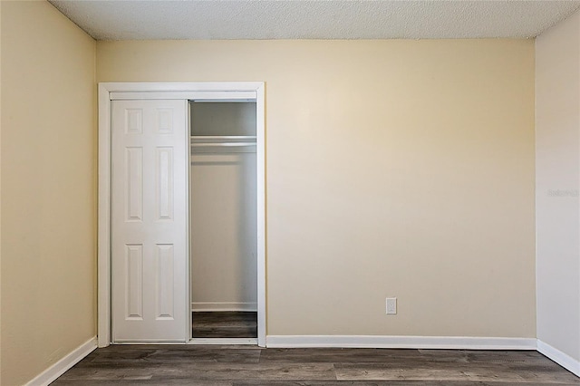 unfurnished bedroom featuring dark wood-type flooring, a closet, a textured ceiling, and baseboards