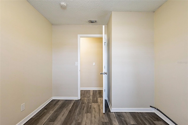 unfurnished room featuring baseboards, visible vents, dark wood finished floors, and a textured ceiling