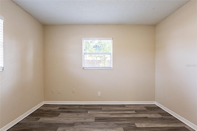 spare room with a textured ceiling, dark wood finished floors, and baseboards