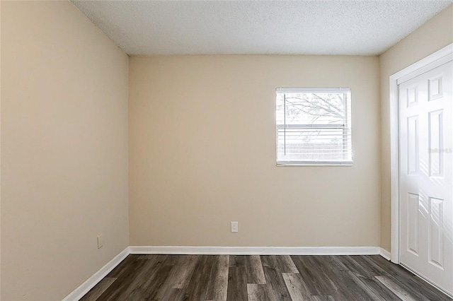 empty room featuring a textured ceiling, dark wood-type flooring, and baseboards