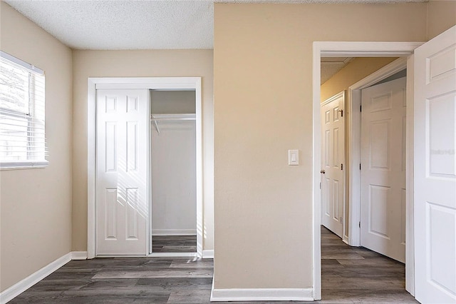 unfurnished bedroom featuring a closet, a textured ceiling, baseboards, and wood finished floors