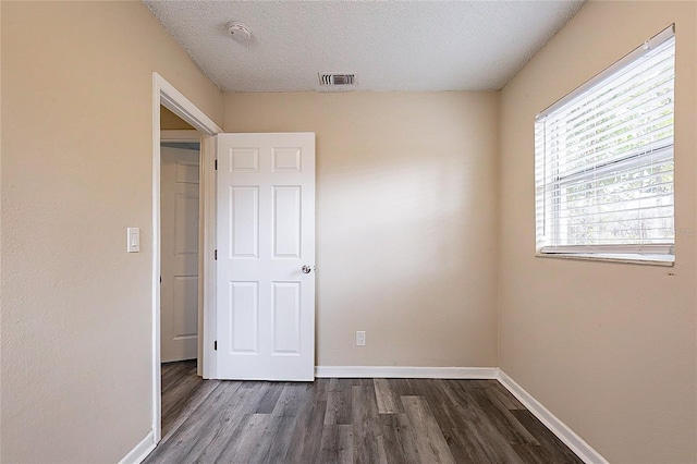 spare room with dark wood-style floors, a textured ceiling, visible vents, and baseboards