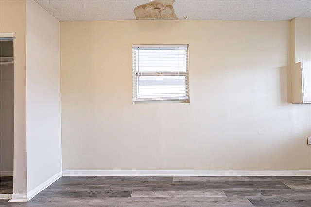 empty room featuring dark wood-type flooring, a textured ceiling, and baseboards