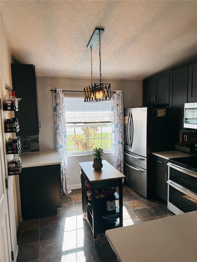 kitchen with dark cabinetry, light countertops, stone tile floors, and appliances with stainless steel finishes