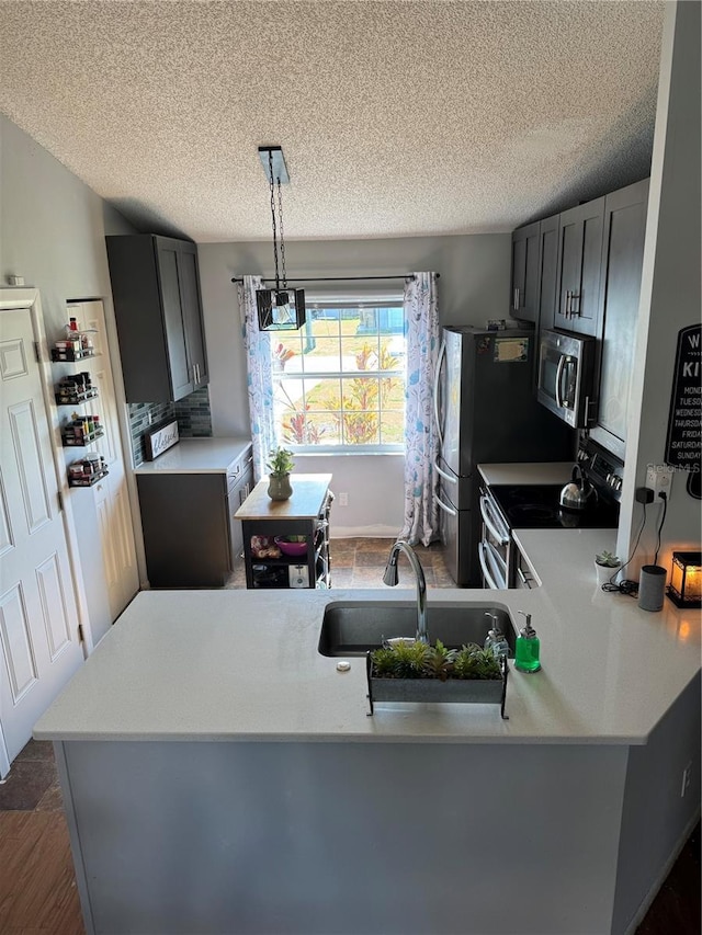 kitchen with a sink, hanging light fixtures, light countertops, appliances with stainless steel finishes, and a textured ceiling