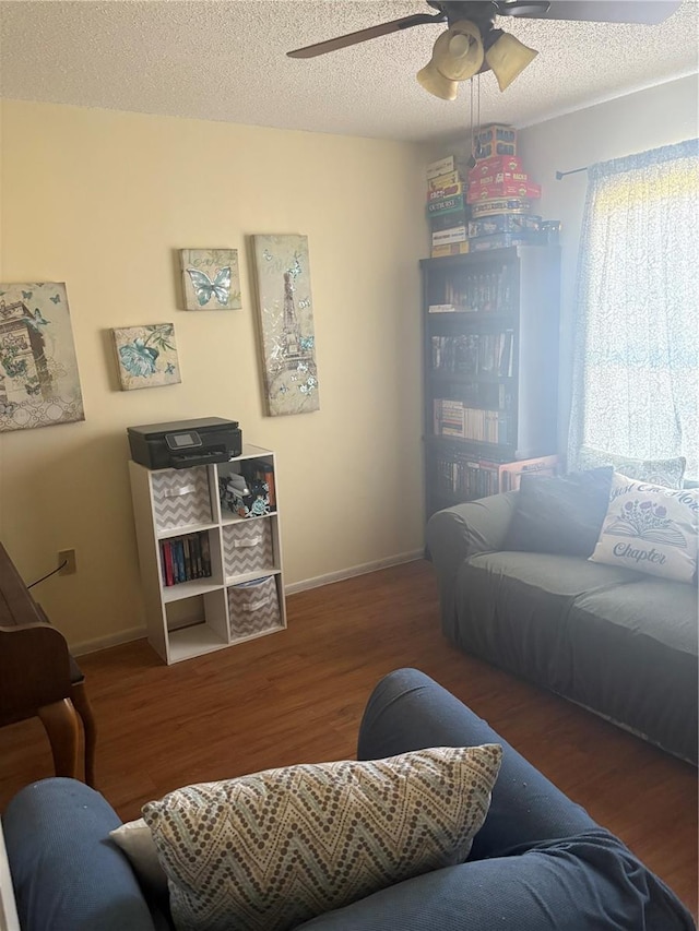 living area featuring baseboards, a textured ceiling, wood finished floors, and a ceiling fan