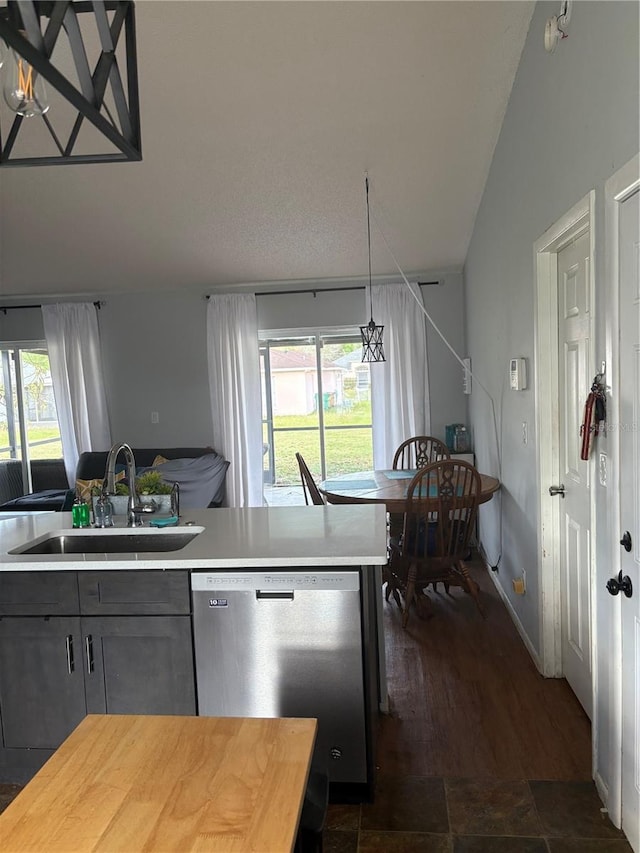 kitchen featuring gray cabinetry, a sink, stainless steel dishwasher, open floor plan, and vaulted ceiling