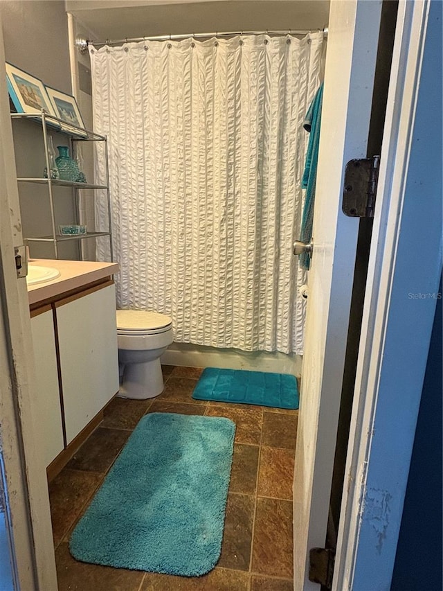 full bathroom featuring curtained shower, toilet, vanity, and stone finish floor