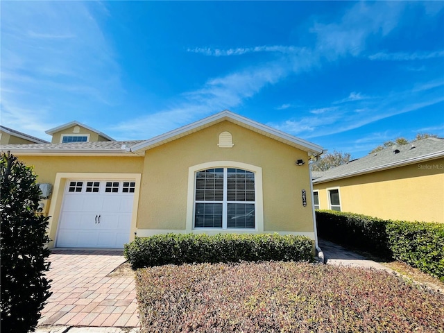 ranch-style house with a garage, decorative driveway, and stucco siding