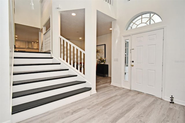 foyer entrance with baseboards, stairs, a high ceiling, light wood-type flooring, and recessed lighting