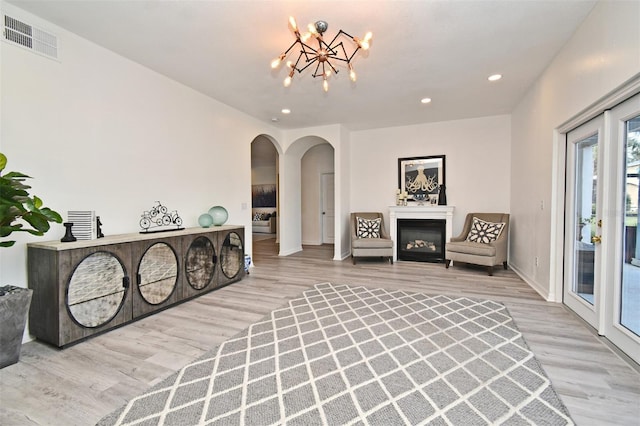 living area featuring light wood finished floors, visible vents, arched walkways, a glass covered fireplace, and a chandelier