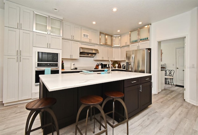 kitchen featuring a center island with sink, a breakfast bar area, appliances with stainless steel finishes, glass insert cabinets, and extractor fan