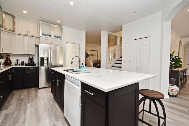 kitchen with a center island with sink, glass insert cabinets, white dishwasher, stainless steel refrigerator with ice dispenser, and a sink