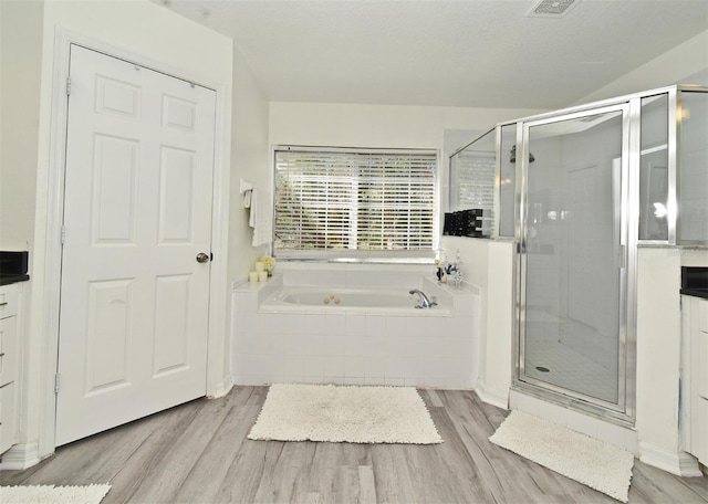 full bathroom with a bath, a shower stall, a textured ceiling, and wood finished floors