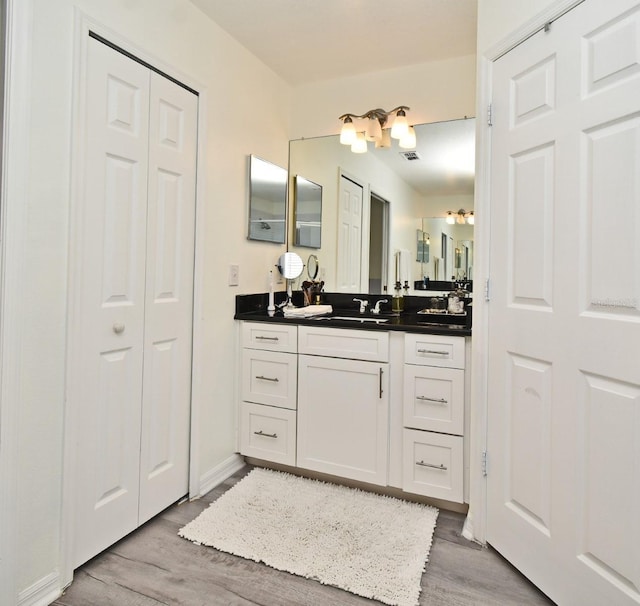 bathroom with a closet, visible vents, vanity, and wood finished floors