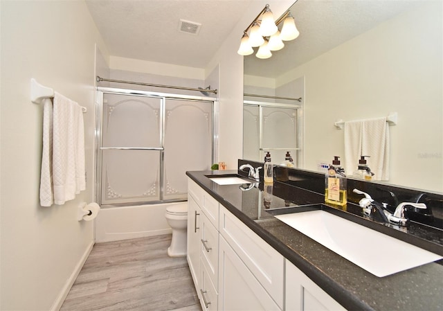 bathroom with visible vents, bath / shower combo with glass door, a sink, and wood finished floors