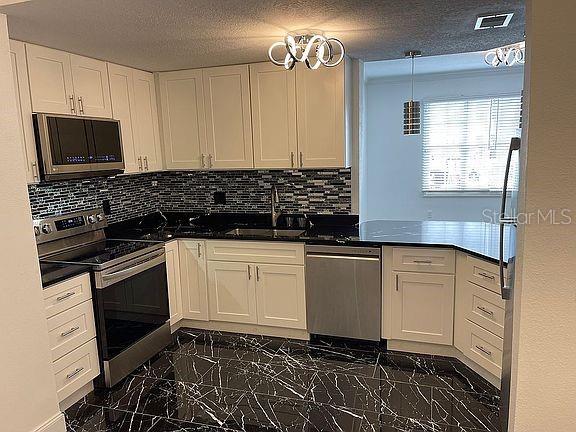 kitchen with decorative light fixtures, marble finish floor, stainless steel appliances, white cabinetry, and a sink