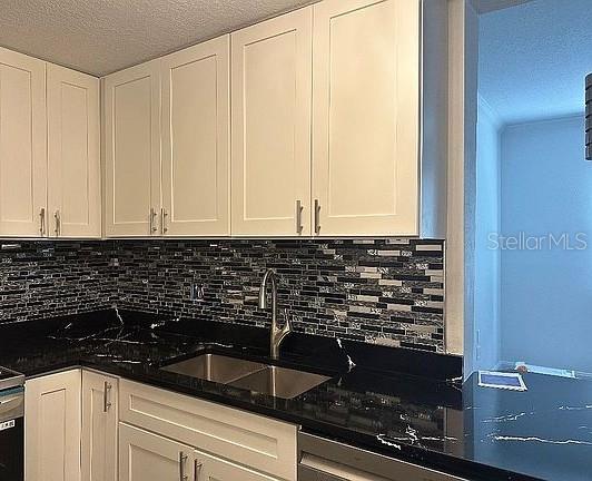 kitchen with a textured ceiling, white cabinetry, decorative backsplash, and a sink