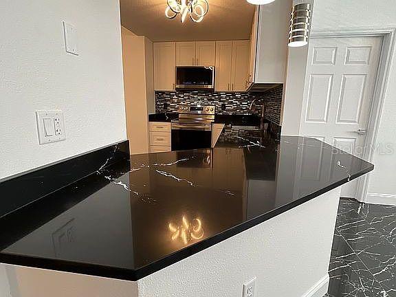 kitchen with a sink, marble finish floor, appliances with stainless steel finishes, backsplash, and dark countertops