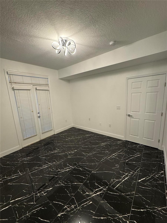 unfurnished room featuring marble finish floor, baseboards, and a textured ceiling