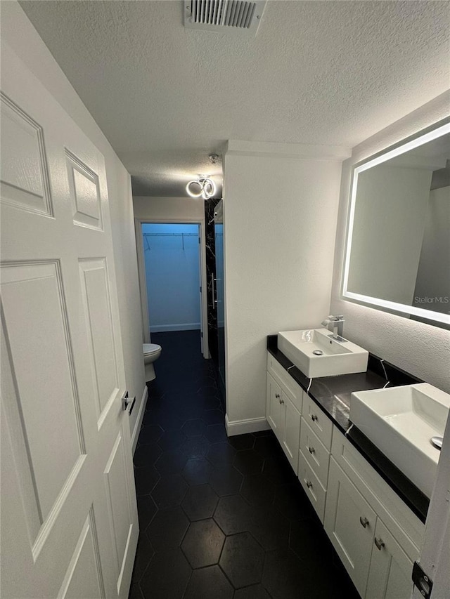 full bath featuring toilet, a sink, visible vents, double vanity, and a walk in closet