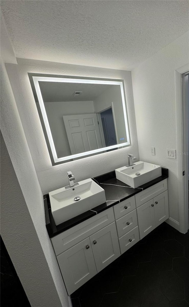 bathroom with a textured wall, a sink, a textured ceiling, and double vanity