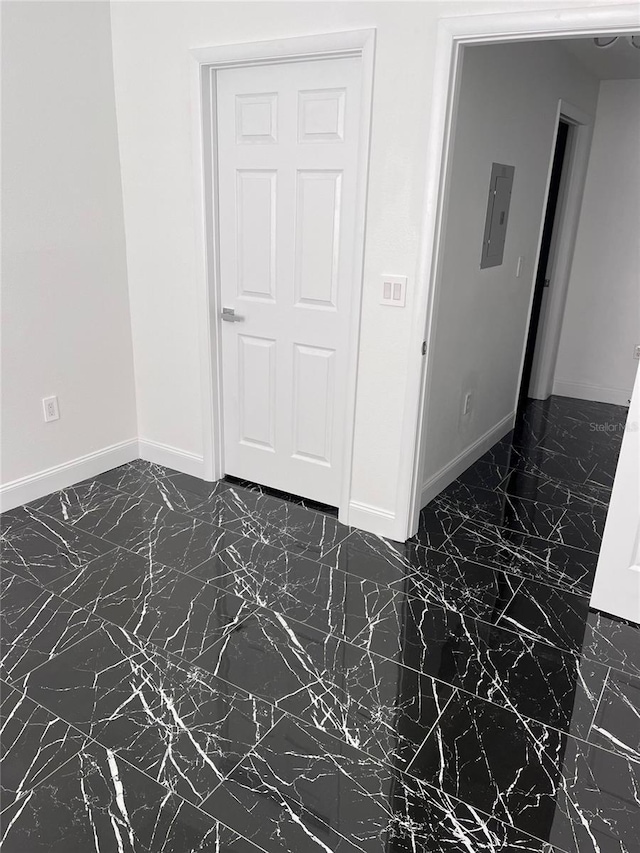 empty room featuring marble finish floor, electric panel, and baseboards