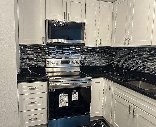 kitchen featuring stainless steel appliances, dark stone countertops, backsplash, and white cabinetry