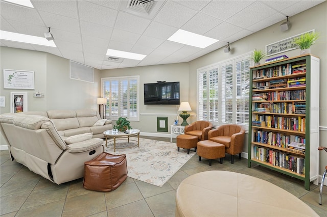 living area featuring a paneled ceiling, tile patterned flooring, visible vents, and baseboards