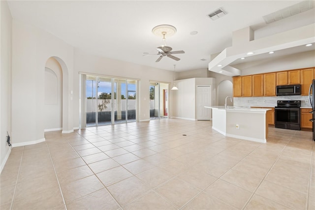 unfurnished living room with ceiling fan, light tile patterned floors, arched walkways, a sink, and visible vents