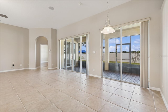 empty room featuring arched walkways, baseboards, and light tile patterned floors