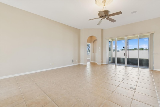 spare room featuring arched walkways, light tile patterned flooring, ceiling fan, and baseboards