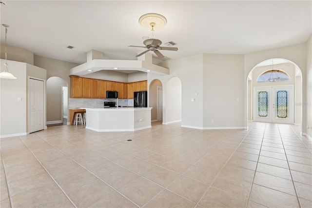 unfurnished living room featuring a ceiling fan, arched walkways, light tile patterned flooring, and visible vents